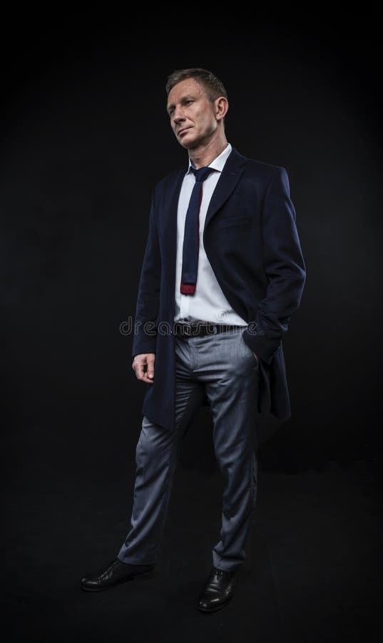 Eleganter moderner Mann in einem Hemd und in einem Mantel auf der Stellung auf einem schwarzen Hintergrund lizenzfreies stockfoto