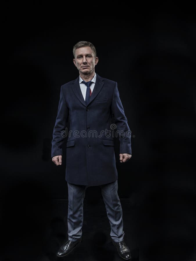 Eleganter moderner Mann in einem Hemd und in einem Mantel auf der Stellung auf einem schwarzen Hintergrund lizenzfreie stockbilder