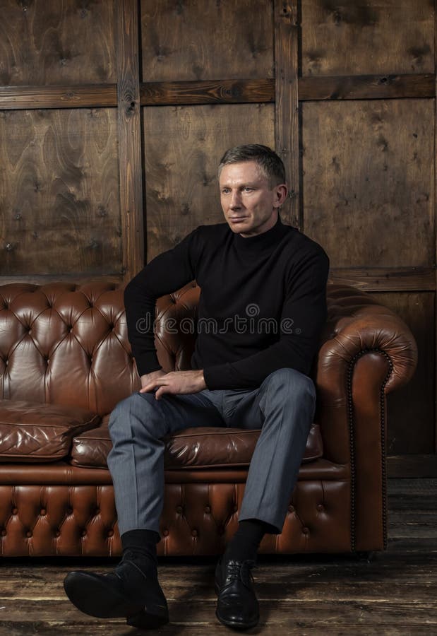 Eleganter moderner Mann in einer schwarzen Strickjacke sitzt auf einem ledernen Sofa