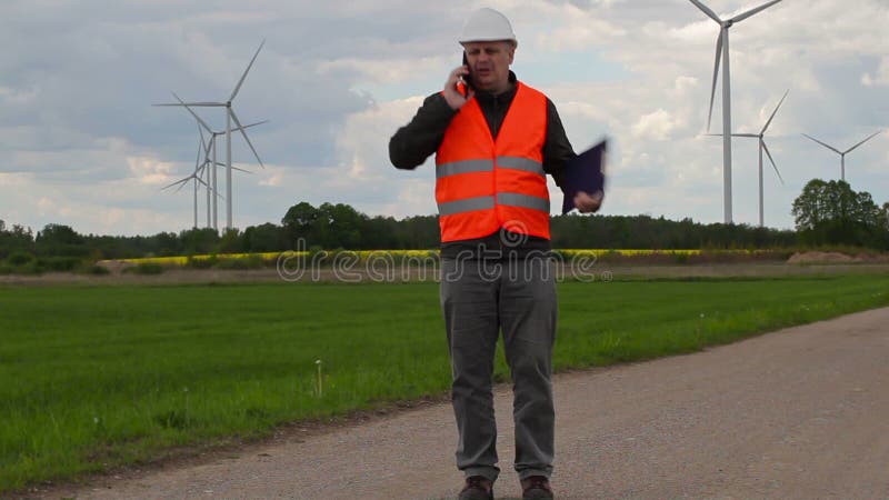 Elektrikeringenieur, der am intelligenten Telefon nahe Windmühlen geht und spricht stock video footage