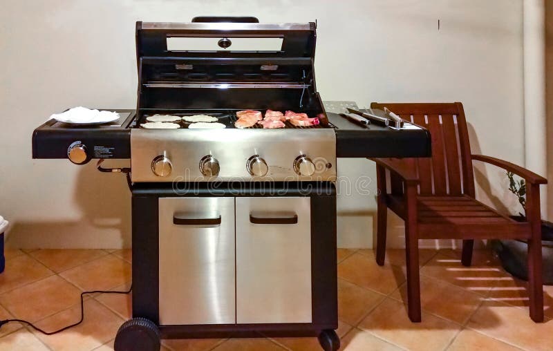 An Electric grill on tile patio against stucco wall with meat and flatbread and cooking tools ready to go. An Electric grill on tile patio against stucco wall with meat and flatbread and cooking tools ready to go