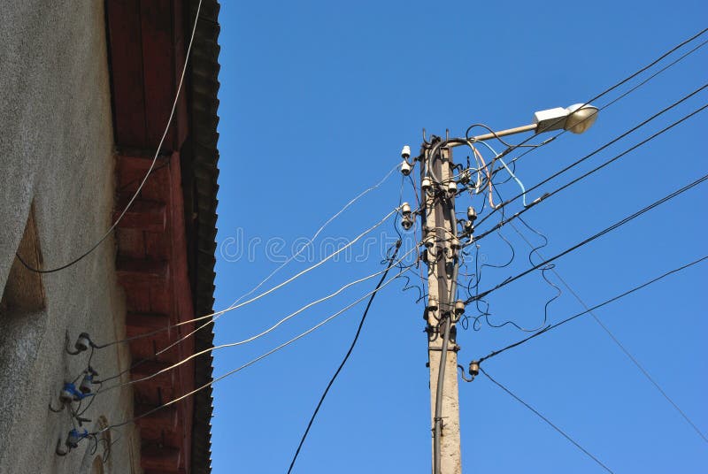 Elektryczni ceramiczni lonty i czerń druty pod łupkowym dachem na lampionie ściennym i starym, widok od ziemi nakrywać, niebieski fotografia stock Elektryczni ceramiczni lonty i czerń druty pod łupkowym dachem na lampionie ściennym i starym, widok od ziemi nakrywać, niebieski fotografia stock