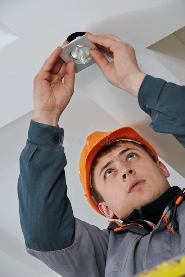 Electrician worker in uniform installing or replacing spot light lamp into ceiling. Electrician worker in uniform installing or replacing spot light lamp into ceiling