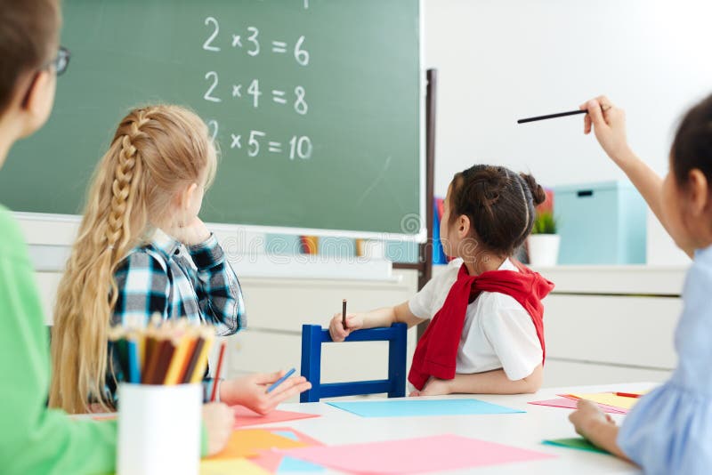 Elementary school kids sitting in classroom and looking at blackboard with multiplication sums. Elementary school kids sitting in classroom and looking at blackboard with multiplication sums