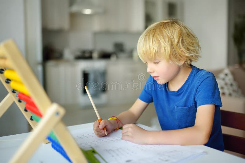 Elementary student boy doing homework at home. Child learning to count, solves arithmetic examples, doing exercises in workbook. Math tutorial. Preparing preschooler baby for school. Education for kids