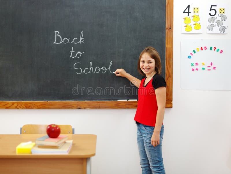 Elementary school girl writing Back to School on chalkboard. Elementary school girl writing Back to School on chalkboard