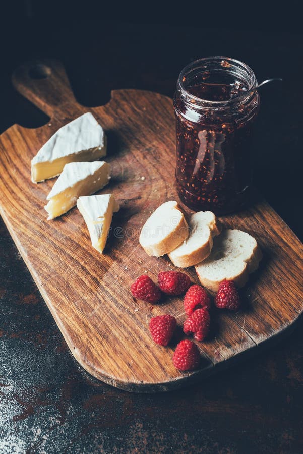 elevated view of brie, raspberries, jam in jar and baguette on cutting board stock image elevated view of brie, raspberries, jam in jar and baguette on cutting board stock image
