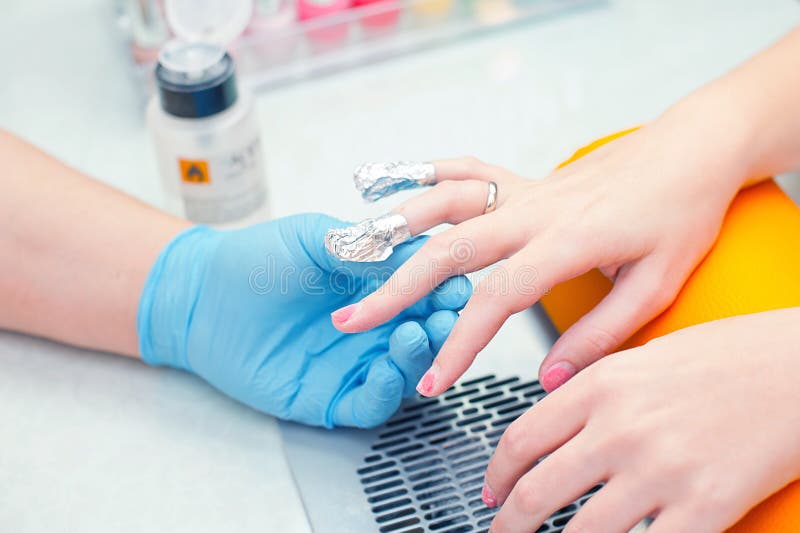 Removing old hybrid manicure in beauty salon using acetone and aluminum foil caps. Removing old hybrid manicure in beauty salon using acetone and aluminum foil caps.