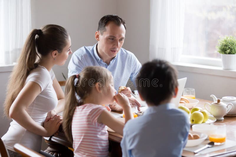 Eltern, die Computer während Kinder essen Frühstück an der Küche aufpassen lizenzfreies stockbild