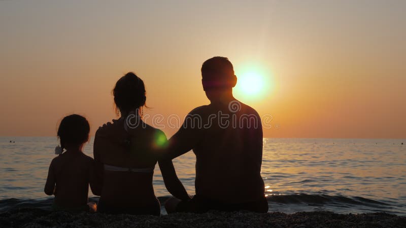 Eltern mit ihrem Kind den Sonnenuntergang durch das See- oder Ozeanufer genießen.