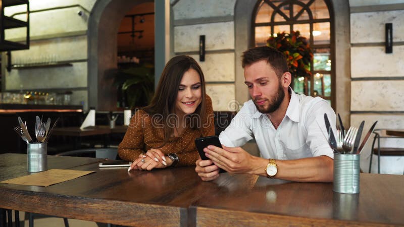 Email emozionante della lettura delle coppie con buone notizie in uno smartwatch in una caffetteria con una finestra nei preceden