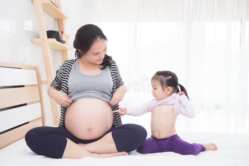 Embarazada y su hija que muestran su vientre en cama foto de archivo Embarazada y su hija que muestran su vientre en cama foto de archivo