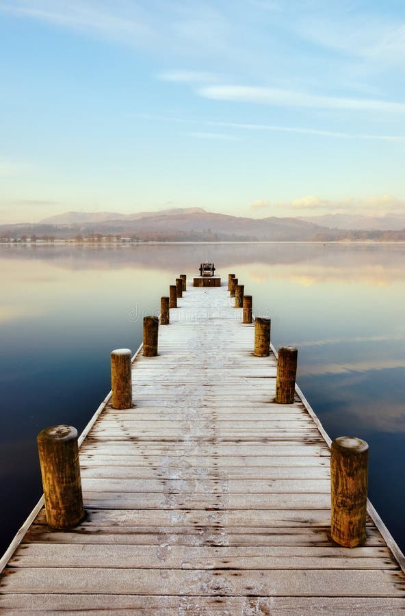 Jetty At Windermere, English Lake District, Cumbria, England, extending out in to a peaceful lake with distant hills. Jetty At Windermere, English Lake District, Cumbria, England, extending out in to a peaceful lake with distant hills.