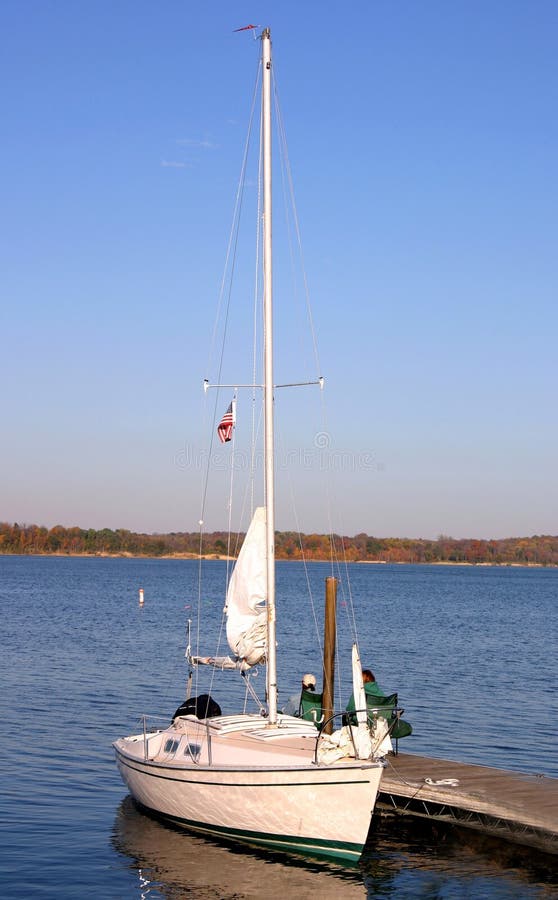 People sitting at end of dock with sail boat docked. People sitting at end of dock with sail boat docked