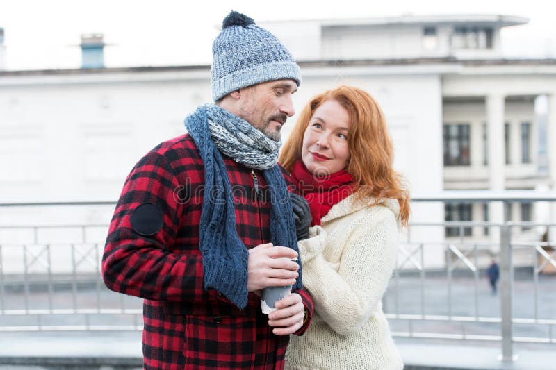 Embarrassed guy with coffee cup in hand. Sweet aged couple meet on street. Woman pleased guy about coffee. Lovely couple walking royalty free stock image Embarrassed guy with coffee cup in hand. Sweet aged couple meet on street. Woman pleased guy about coffee. Lovely couple walking royalty free stock image