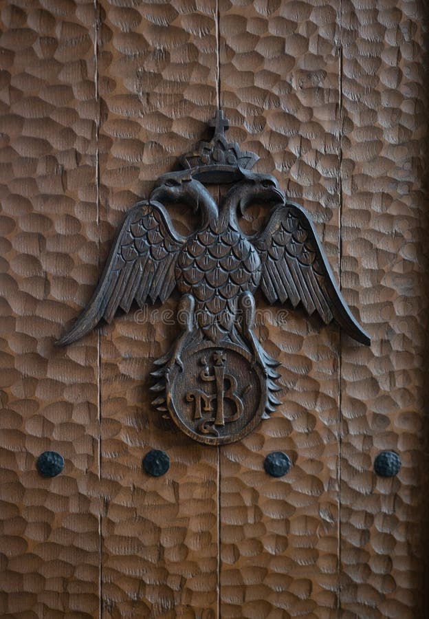 A double-headed eagle with outstretched wings wearing a crown with cross on a hammered wood door. A double-headed eagle with outstretched wings wearing a crown with cross on a hammered wood door