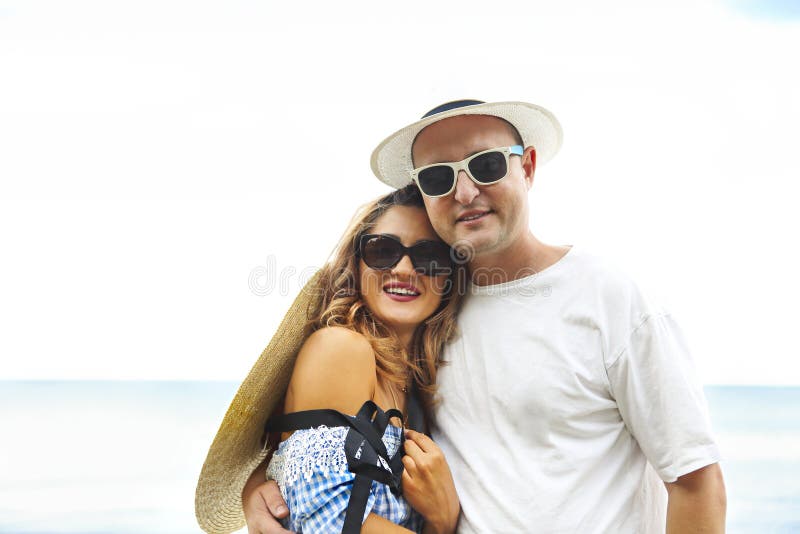 Embracing young couple in sunglasses, hats on a beach with blue sea on background royalty free stock photography Embracing young couple in sunglasses, hats on a beach with blue sea on background royalty free stock photography