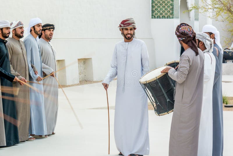 Emirati-Männer, die das Yowla, einen traditionellen Tanz im Erbe Arabische Emirates nahe bei einem historischen Gebäude durchführ stockfotografie Emirati-Männer, die das Yowla, einen traditionellen Tanz im Erbe Arabische Emirates nahe bei einem historischen Gebäude durchführ stockfotografie