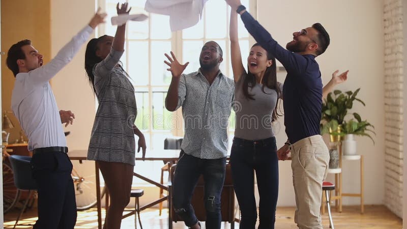 Emocionado equipo de negocios diverso lanzando papeles bailando en la oficina metrajes