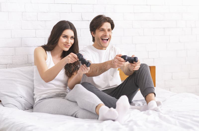 Emocjonalni millennials bawić się gra wideo, siedzi z joystickiem na łóżku fotografia stock Emocjonalni millennials bawić się gra wideo, siedzi z joystickiem na łóżku fotografia stock