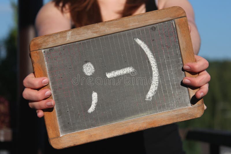 Emoticon sketched with chalk on slate shown by young female