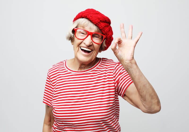 Lifestyle, emotion and people concept: Funny old lady wearing red hat and e...