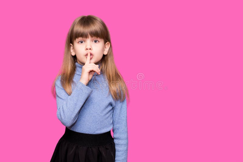 Emotional child girl has secret. Little girl with wonder face keeps finger on lips, shows silence sign, asks to be quiet and stop