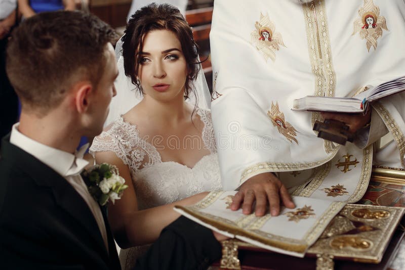 Emotional couple at wedding ceremony in christian catholic church, taking vows with priest and holy bible at the altar, faces