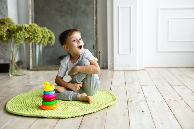 Emotional little child boy is surprised of toy pyramid on knitted carpeet on the wooden floor indoor. Knitted style in the