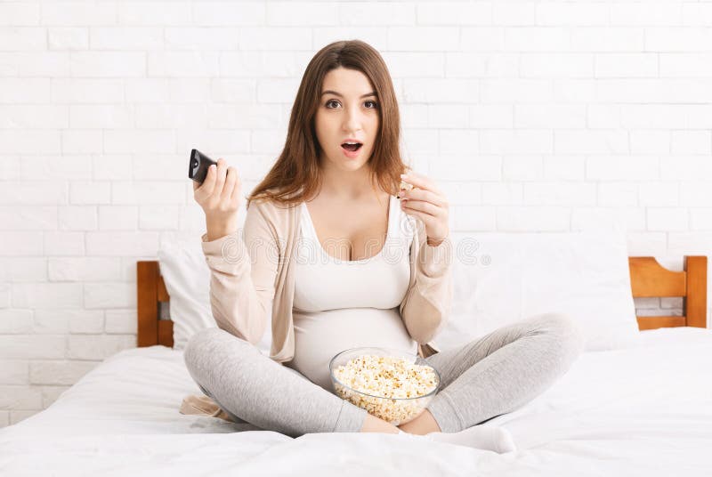 Emotional pregnant woman watching TV, eating popcorn