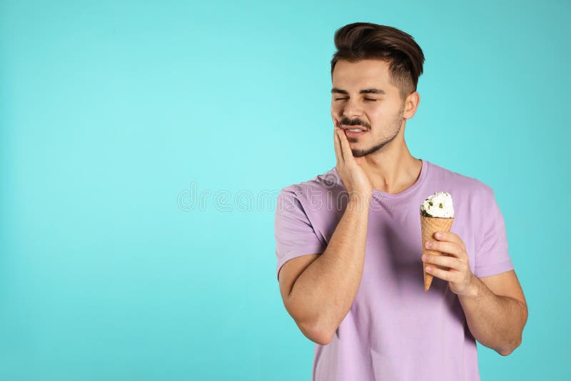 Emotional young man with sensitive teeth and ice cream on color background.