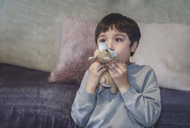 Emotional portrait kid raising eyebrows and covering his mouth with dog toy being surprised and shocked while watching TV, Surprised cute young boy child looking up with wondering face. Emotional portrait kid raising eyebrows and covering his mouth with dog toy being surprised and shocked while watching TV, Surprised cute young boy child looking up with wondering face