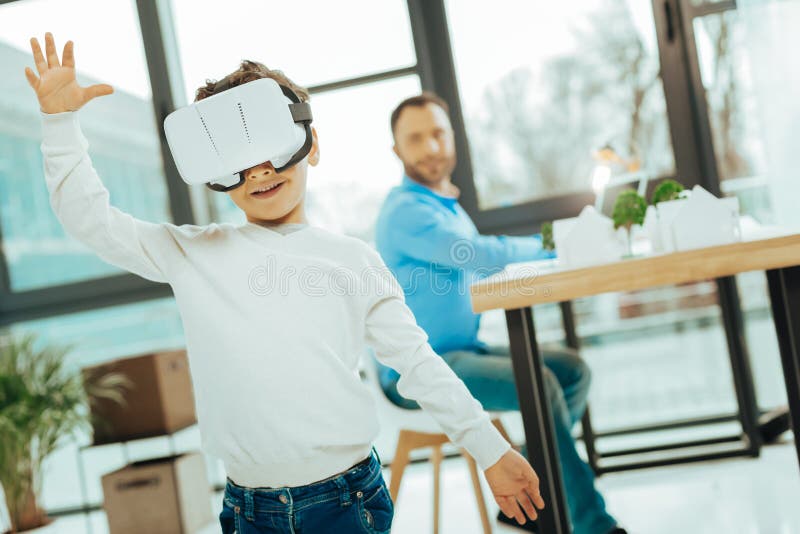 Emotionell pojke som sätter hans händer upp, medan genom att använda virtuell verklighetexponeringsglas arkivfoto