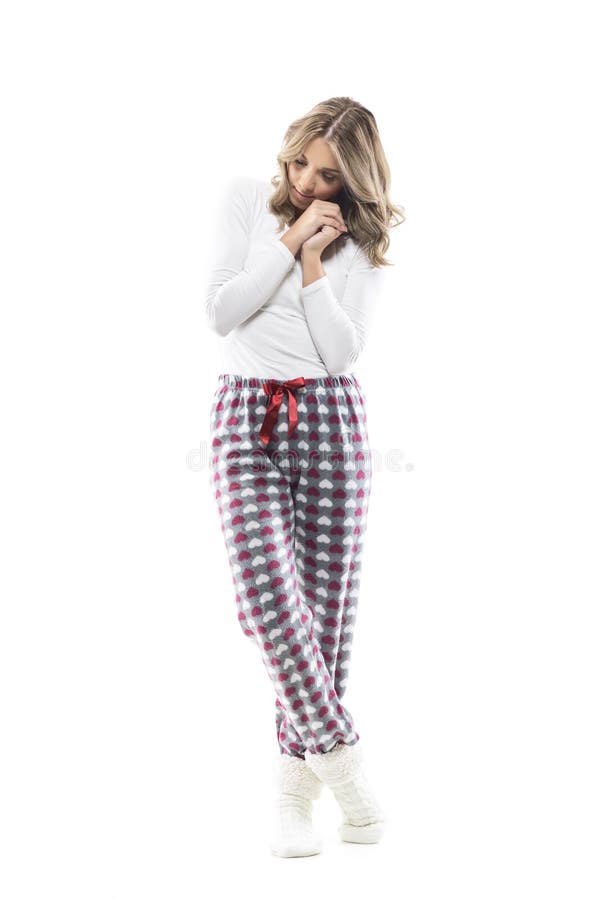 Emotional young thoughtful woman in pajama and socks looking down holding hands against cheek. Full length portrait on white background. Emotional young thoughtful woman in pajama and socks looking down holding hands against cheek. Full length portrait on white background