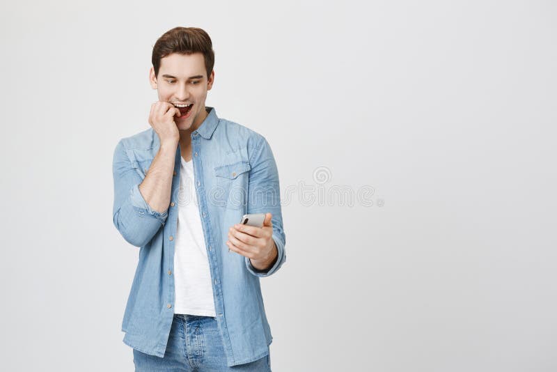 Emotive young cute student with surprised and amazed expression looking at smartphone biting fingers and smiling royalty free stock photos Emotive young cute student with surprised and amazed expression looking at smartphone biting fingers and smiling royalty free stock photos