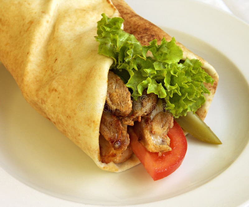 A close up view of a middle eastern style charwama sandwich. Sometimes spelled, Sharwama, Shoarma or Shaorma. Made from shaved lamb, goat or chicken meat, less often with turkey or beef. Wrapped in pita bread and served with lettuce and tomato on a plate. A close up view of a middle eastern style charwama sandwich. Sometimes spelled, Sharwama, Shoarma or Shaorma. Made from shaved lamb, goat or chicken meat, less often with turkey or beef. Wrapped in pita bread and served with lettuce and tomato on a plate.