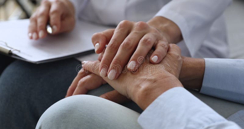 Empatisk, ung sjuksköterska med handstöd till äldre patienter.