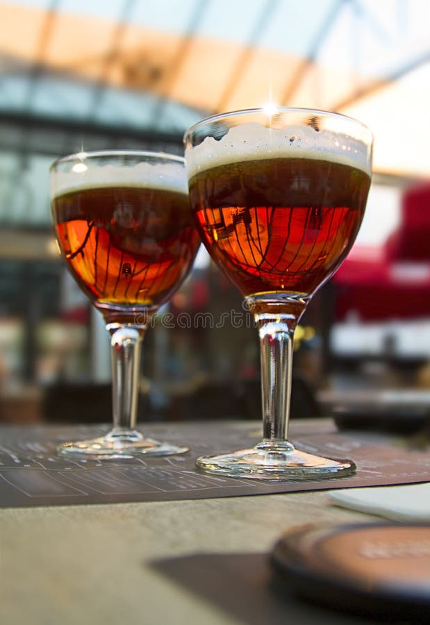 Empañe el fondo ligero con dos vidrios de cerveza oscura en la tabla del café imagen de archivo Empañe el fondo ligero con dos vidrios de cerveza oscura en la tabla del café imagen de archivo