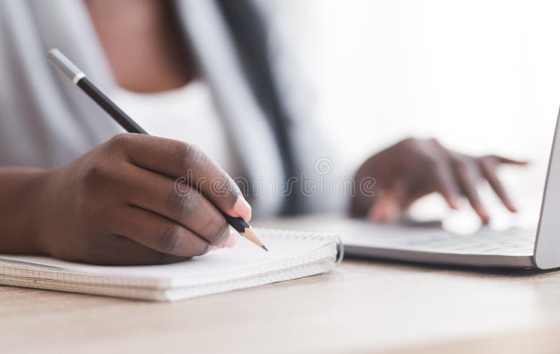 Empleada mujer irreconocible que toma notas mientras trabaja en una laptop en la oficina