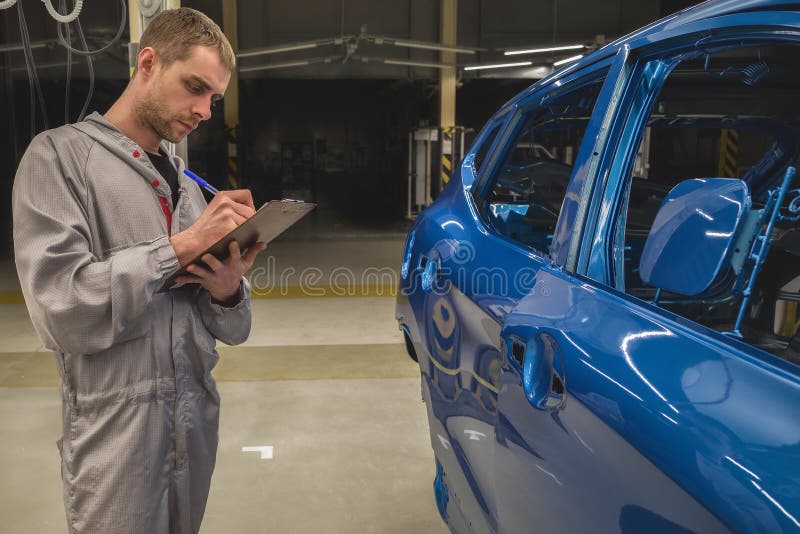 An employee in the car body painting shop writes notes about production defects. An employee in the car body painting shop writes notes about production defects