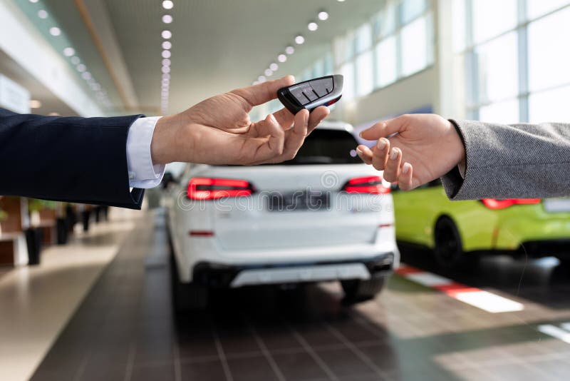 an employee of a car store handing over the keys to a new car to a buyer close-up against the backdrop of the showroom.