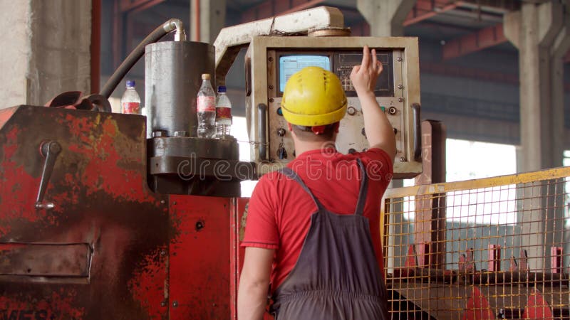An employee in helmet operating a metal processing machine that manufactures sheet metal for further processing. Mechanical technician operating program on control panel in factory. Concept for industrial worker, manual work and manufacturing