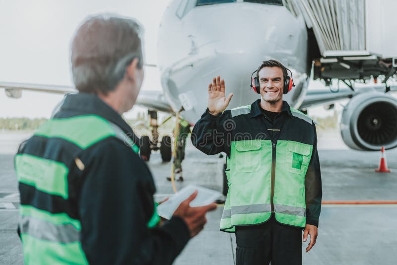 Employé bel de sourire dans des mains de ondulation d'écouteur rouge au mécanicien photos stock