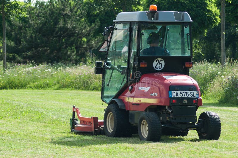 Employé municipal conduisant le tracteur et la tondeuse à gazon rouges, pelouses de cisaillements en parc urbain photographie stock Employé municipal conduisant le tracteur et la tondeuse à gazon rouges, pelouses de cisaillements en parc urbain photographie stock
