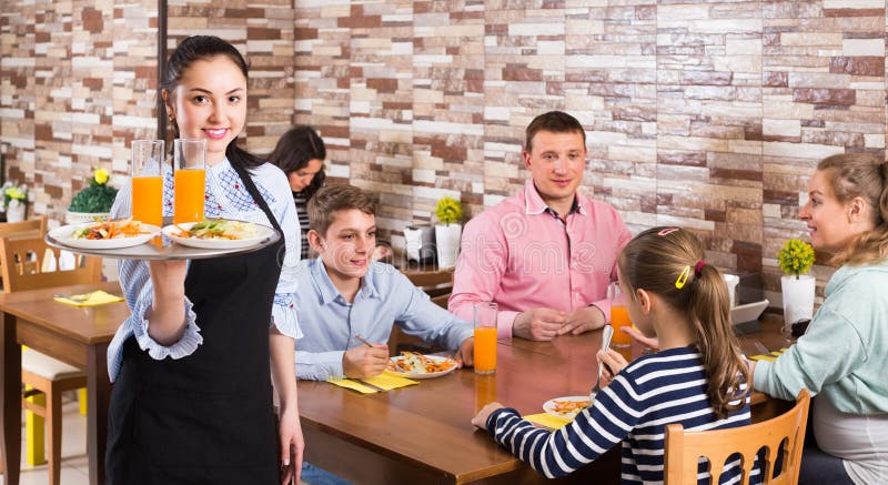 A empregada de mesa nova amigável dá-lhe boas-vindas ao café da família fotografia de stock A empregada de mesa nova amigável dá-lhe boas-vindas ao café da família fotografia de stock