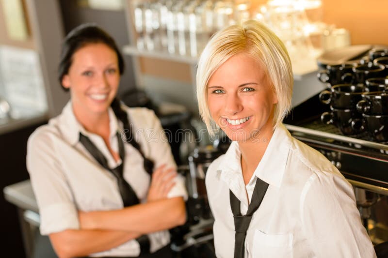 Empregadas de mesa do café atrás da barra que sorriem no trabalho