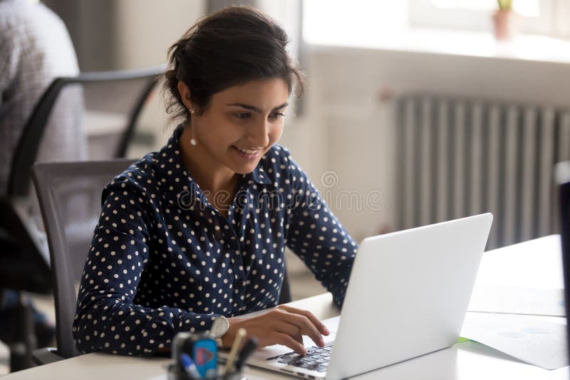 Empregado do sexo feminino indiano de sorriso que usa o portátil no local de trabalho