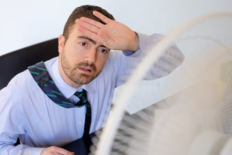 Flushed employee feeling hot in front of a fan. Flushed employee feeling hot in front of a fan