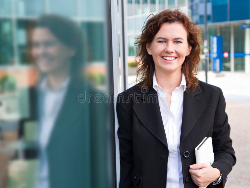 Empresaria confiada joven con la carpeta cerca de la estructura de la oficina imagen de archivo Empresaria confiada joven con la carpeta cerca de la estructura de la oficina imagen de archivo