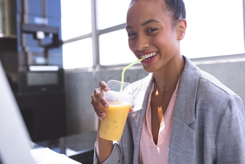 Empresaria que come batido de leche mientras que trabaja en el ordenador en el escritorio imagen de archivo Empresaria que come batido de leche mientras que trabaja en el ordenador en el escritorio imagen de archivo